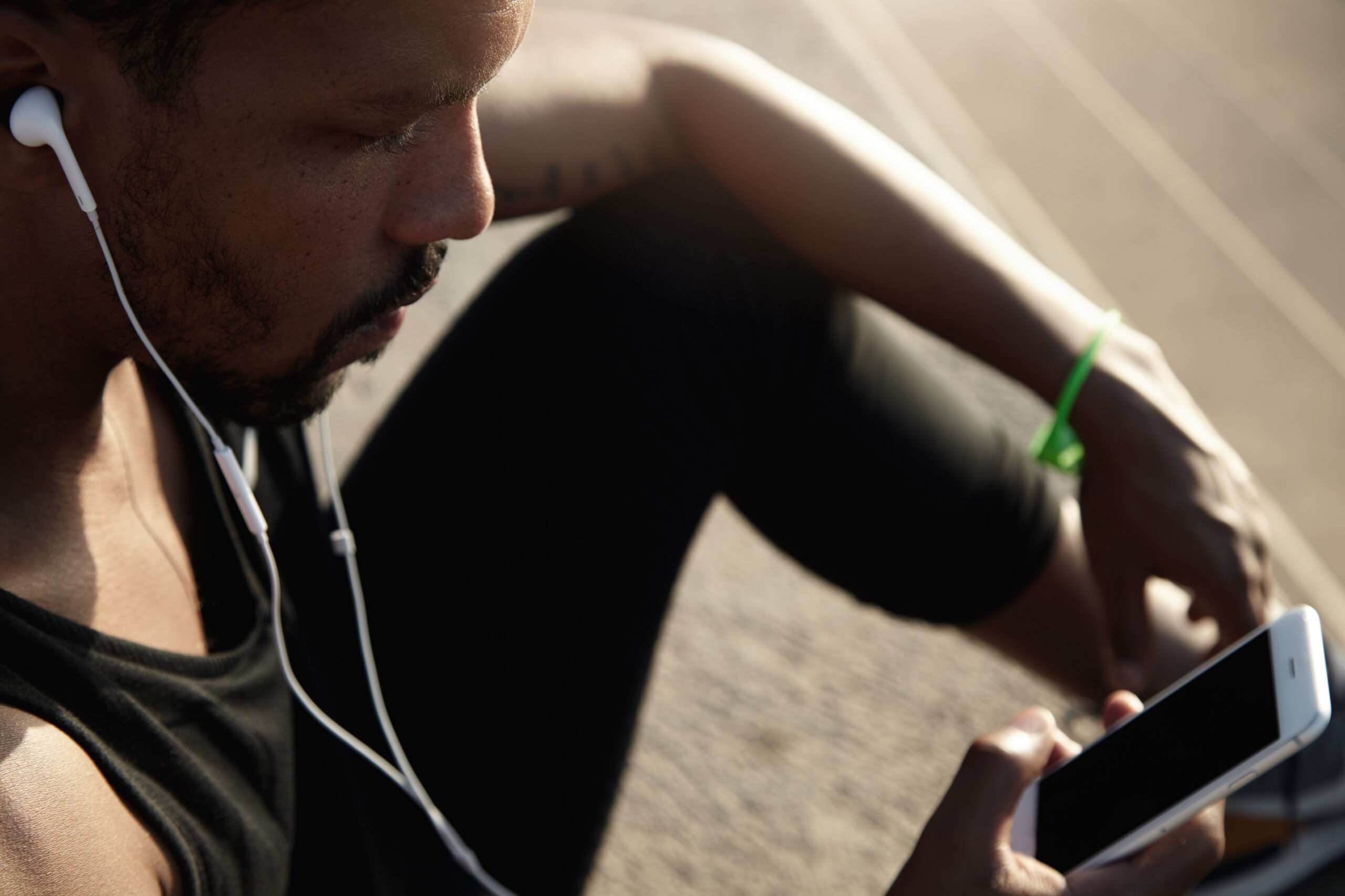 Human and technology concept. People and sport. Handsome African guy in headphones listening to music using his smart phone with blank copy space screen for your advertising text or information